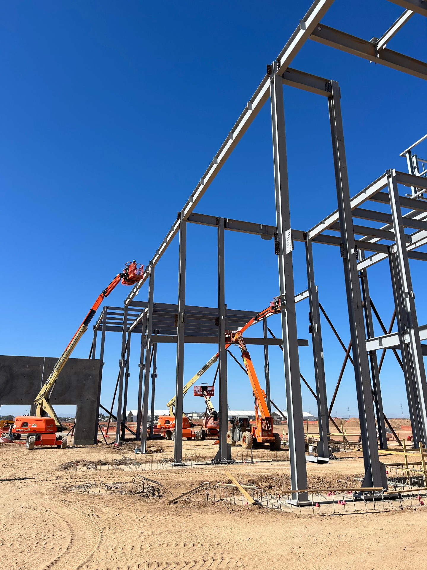 Tall multi-bay steel frame with boom lifts under a clear blue sky in Phoenix, Arizona